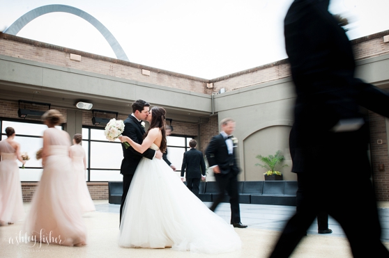 Photo of the wedding party walking around the couple while they are standing still kissing