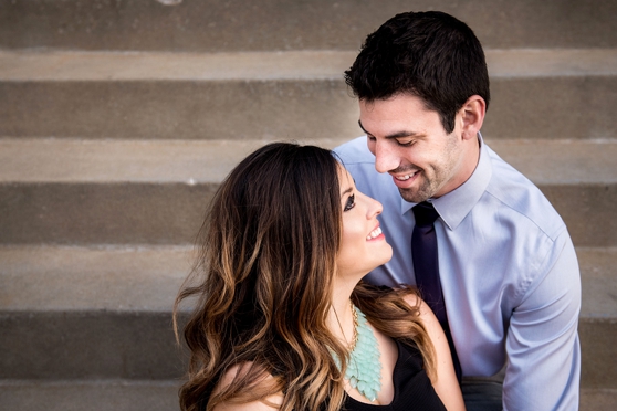 Photo of couple sitting on concrete stairs smiling at each other in downtown Clayton engagement session