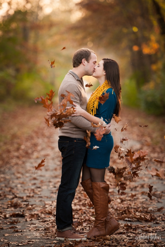 Photo of couple throwing fall leaves and kissing on trail