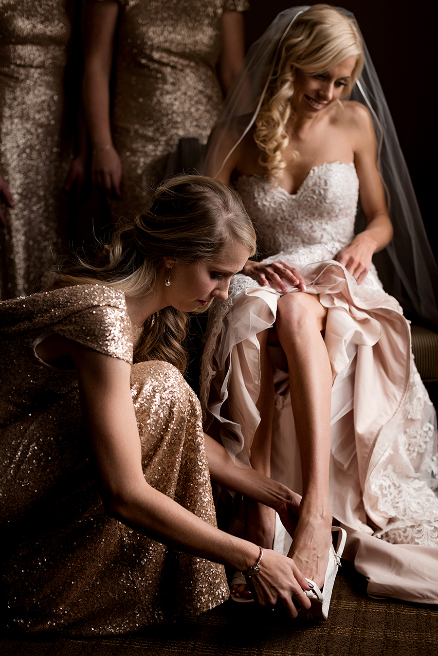 bridesmaid helping the bride put her shoes on for a winter wedding at graham chapel by ashley fisher photography