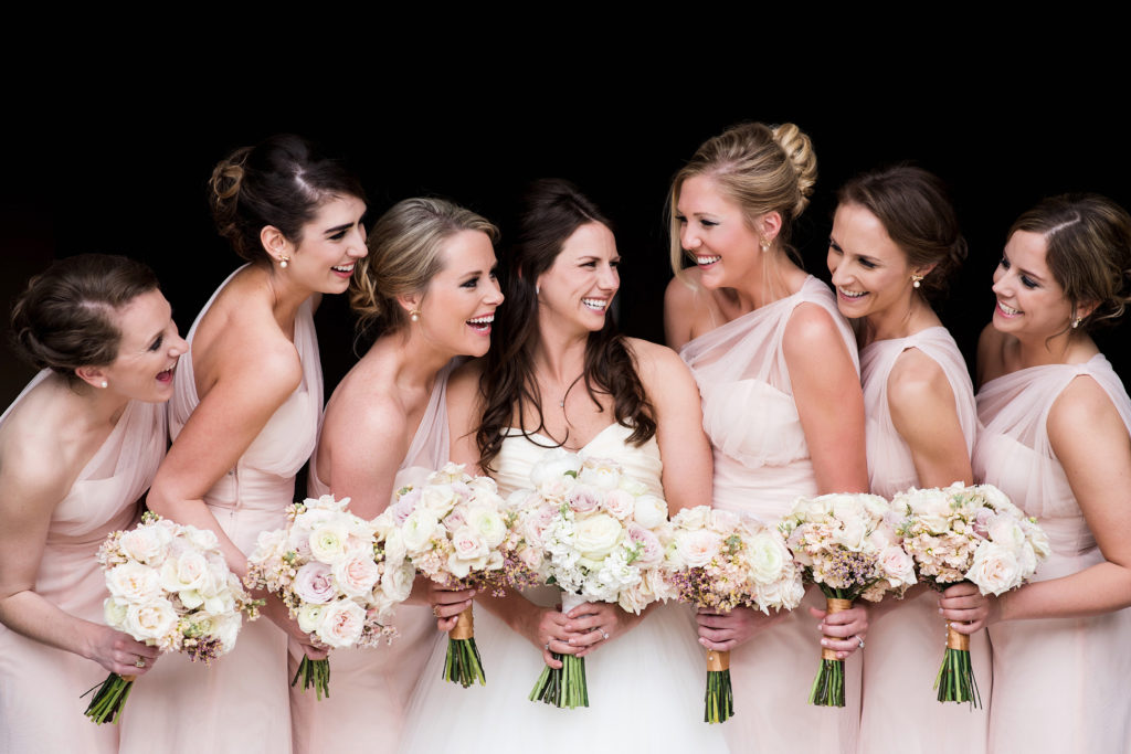 bride and bridesmaids in pink one-shoulder dresses laughing with each other