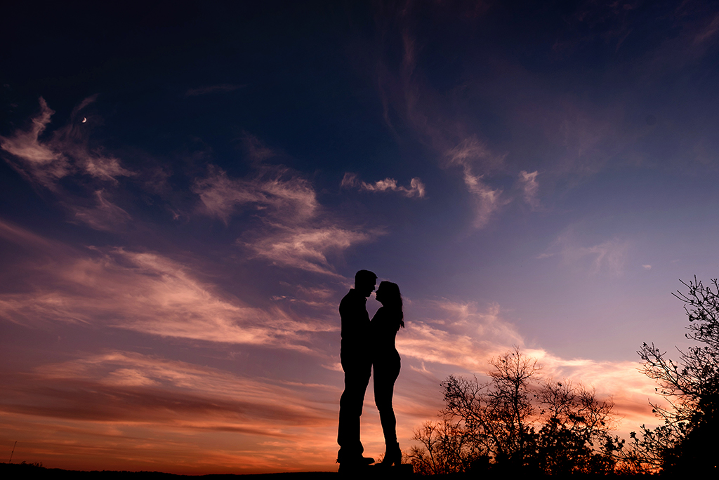 silhouette of couple among purple, pink, and orange sky with moon and clouds during fall elephant rock state park engagement session