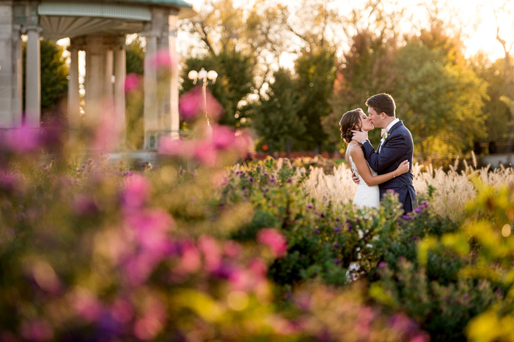 sunset portrait of couple kissing at the muny in st louis, shot through pink flowers and fall foliage
